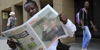 A pedestrian sits and reads a copy of the Sowetan daily newspaper with a front page photograph of the former South African President Nelson Mandela following the announcement of his death in Johannesburg, South Africa, on Friday, Dec. 6, 2013. Mandela, the freedom fighter who emerged from 27 years in prison to become South Africa's first elected black president and a global symbol of reconciliation, died at his home in Houghton aged 95. Photographer: Dean Hutton/Bloomberg via Getty Images