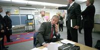 U.S. President George W. Bush (C) makes a telephone call as White House Director Of Communications Dan Bartlett points to video footage of the terrorist attack on the World Trade Center from Emma Booker Elementary School September 11, 2001 in  Sarasota, Florida.  (Photo by Eric Draper/White House/Getty Images)