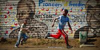 Children run past a mural of former South African president Nelson Mandela and other freedom fighters in the Orlando District of Soweto Township on June 30, 2013 in Johannesburg, South Africa. People continue to gather and lay flowers and tributes outside the Mediclinic Heart Hospital where Mandela is being treated for a lung infection on his 23rd day in hospital.  (Photo by Jeff J Mitchell/Getty Images)