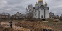 epaselect epa09874758 A member of the Ukrainian army stands next to a mass grave in front of an Orthodox church, in Bucha, northwest of Kyiv, Ukraine, 06 April 2022. Hundreds of tortured and killed civilians have been found in Bucha and other parts of the Kyiv region after the Russian army retreated from those areas. Russian troops entered Ukraine on 24 February resulting in fighting and destruction in the country, and triggering a series of severe economic sanctions on Russia by Western countries.  EPA-EFE/ROMAN PILIPEY ATTENTION: GRAPHIC CONTENT