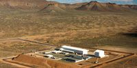 An arial view of the underground Karoo Array Processing Building (grey building) of MeerKAT and the Square Kilometre Array (SKA-Mid); the dish assembly shed (long white building) and the pedestal assembly shed (behind it). The mound to the left of the picture is manmade  and helps to keep radio frequency interference out and so does the mountains. (Photo: SARAO)