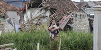 epa10326705 A villager carries her child as she walks past a collapsed house affected by the 5.6 magnitude earthquake in Cianjur, Indonesia, 25 November 2022. According to the National Disaster Management Authority (BNPB), at least 272 people killed after 5.6 magnitude earthquake hit southwest of Cianjur, West Java on 21 November 2022.  EPA-EFE/MAST IRHAM