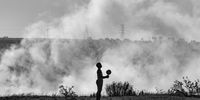 A child plays with a ball near a veldfire in Phola, Mpumalanga. (Photo: Daylin Paul)<br>