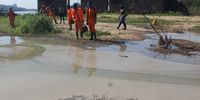 River rehabilitation workers, including Nduduzo Ndaba and Siboniso Lehoma (centre) are reflected in the surface of the fetid, sewage-polluted water next to the Umgeni River. (Photo: Tony Carnie)<br>