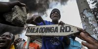 A protester points to a sign with the name of Azimio coalition party Raila Odinga as protesters and supporters of the opposition Azimio coalition burn tyres as they engage with riot police in running battles, during the renewed nationwide protests in Mathare, Nairobi, Kenya, 19 July 2023. Fresh nation-wide protests against the Kenyan government have been called by the Opposition coalition Azimio over high cost of living and new tax increases, that have been termed as punitive despite a court order stopping its implementations.  EPA-EFE/DANIEL IRUNGU