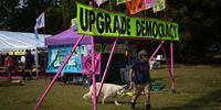 WINDSOR, ENGLAND - AUGUST 30: An Extinction Rebellion supporter walks his dog under a banner in a recently erected camp at Home Park on August 30, 2024 in Windsor, England. Extinction Rebellion's weekend comprises a series of actions and training, including theatrical protests, letters written to King Charles III, a community assembly, and culminates in a march and rally calling for climate justice. The event aims to highlight the need for "citizens' assemblies," which bring together representatives of randomly selected citizens to make informed and actionable decisions about environmental issues. (Photo by Carl Court/Getty Images)