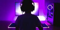 Gamer plays the game on a PC. View from the back. Low light scene with purple back light