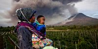 SIMPANG EMPAT, NORTH SUMATRA, INDONESIA - JANUARY 08: A woman carries her son as they watch Mount Sinabung spew pyroclastic smoke on January 8, 2014 in Karo District, North Sumatra, Indonesia. The number of displaced people has increased to 22,000 in Western Indonesia as Mount Sinabung continues to spew ash and smoke after several eruptions since September. Eleven deaths have now been recorded as a result of the eruptions with hundreds more falling ill. Officials expect the number of evacuees to rise as volcanic activity remains high. (Photo by Ulet Ifansasti/Getty Images)