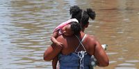 A resident carries a baby as she walks through a flooded street after the rains of the last two days, in the municipality of Duque de Caxias, in the Baixada Fluminense region, metropolitan area of Rio de Janeiro, Brazil, 15 January 2024. The storm that hit the Brazilian city of Rio de Janeiro and its metropolitan region between Saturday night and early Sunday morning caused the death of at least eleven people and flooded dozens of streets, local authorities reported.  EPA-EFE/ANDRE COELHO