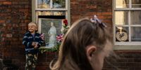 WINDSOR, ENGLAND - SEPTEMBER 17: A kid poses for a picture next to a portrait of Queen Elizabeth II and tributes sitting on the window sill of home near Windsor Castle on September 17, 2022 in Windsor, England. Queen Elizabeth II is lying in state at Westminster Hall until the morning of her funeral to allow members of the public to pay their last respects. Elizabeth Alexandra Mary Windsor was born in Bruton Street, Mayfair, London on 21 April 1926. She married Prince Philip in 1947 and acceded to the throne of the United Kingdom and Commonwealth on 6 February 1952 after the death of her Father, King George VI. Queen Elizabeth II died at Balmoral Castle in Scotland on September 8, 2022, and is succeeded by her eldest son, King Charles III. (Photo by David Ramos/Getty Images)