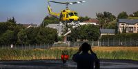 A man films a helicopter collecting water in a dam near Kanonberg Lifestyle Estate. A fire on Tygerberg Hills came close to homes in Cape Town’s northern suburbs on 25 January 2024. (Photo: Shelley Christians)