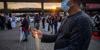 A man holds a lit candle while being addressed by various dignitaries.<br>Photo / Shiraaz Mohamed