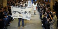 PARIS, FRANCE - OCTOBER 05: (EDITORIAL USE ONLY - For Non-Editorial use please seek approval from Fashion House) A demonstrator holds a banner as models walk the runway during the Louis Vuitton Womenswear Spring/Summer 2022 show as part of Paris Fashion Week on October 05, 2021 in Paris, France. (Photo by Francois Durand/Getty Images)