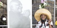 Susan Lewis, a District Six resident, poses next to a photograph of the late anti-apartheid activist Archbishop Emeritus Desmond Tutu who passed away on Sunday 26 December 2021 at the age of 90. (Photo: Leila Dougan)