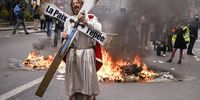 A protester holds a cross with a phrase 'The peace, the sword' as he walks pass by fire during a protest against government pension reform, in Paris, France, 28 March 2023. France faces an ongoing national strike against the government's pensions reform after Prime Minister Elisabeth Borne on 16 March announced the use of article 49 paragraph 3 (49.3) of the Constitution of France to have the text on the controversial pension reform law to be definitively adopted without a vote.  EPA-EFE/YOAN VALAT