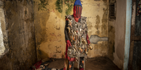 An Egungun in a voodoo convent. He is wearing multiple talismans, which provide him with a strong power. <br>Porto-Novo, Benin. The Egungun association is a secret voodoo society that honours the spirits of their ancestors and perpetuates their memories. These ancestral spirits are believed to be in constant watch over their living relatives; they bless, protect and warn them, but can also punish them depending on whether they remember or neglect them. The spirits can also protect a community against evil spirits, epidemics, witchcraft and evil doers, ensuring their well-being, and may even be invited to come to earth physically. When they do, the Egungun are the receptacles of these spirits, appearing in the streets day or night, leaping, dancing or walking, and uttering loud cries. The spirit is supposed to have returned from the land of the dead to ascertain what is going on, so can be considered a kind of supernatural inquisitor who appears from time to time to inquire into the general domestic conduct of people and punish misdeeds. <br> 