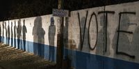 Silhouettes of people queueing for the opening of a polling station appear on a wall where the word ‘vote’ has been spraypainted outside the Matero secondary school in Lusaka on 12 August 2021. (Photo: Marco Longari / AFP)