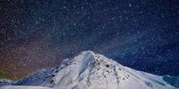 "Stars and Northern Lights Over Chalets, Hatcher Pass, Alaska".<br>Starry skies and a hint of northern lights blaze over a snowy peak and three little chalets in Hatcher Pass, Alaska. © Hal Gage, United States of America, Shortlist, Open, Landscape, 2022 Sony World Photography Awards