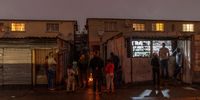 Manenberg residents as seen standing beside a fire while others wait in line at a tuck shop.<br>Photo: Shiraaz Mohamed.