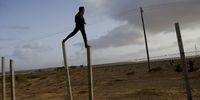 Opposition troops stand atop the pillars of a fence to look out for Libyan government soldiers as the move toward frontline flighting positions, Eastern Libya, March 5, 2011. Dangerous confrontations had been going on between opposition forces and those loyal to Col. Qaddafi across Libya. (Credit: Lynsey Addario for The New York Times)
