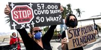 Demonstrators wearing face masks hold signs during a rally against President Jair Bolsonaro and Governor of Rio de Janeiro Wilson Witzel at Copacabana beach on 28 June 2020. (Photo: Andre Coelho / Getty Images)