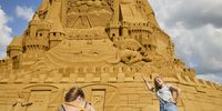 epa09329279 People take pictures at the world's tallest sand sculpture as its under construction in Blokhus, Denmark, 07 July 2021. The Dutch designer Wilfred Stijger is behind the work, which is inspired by the covid-19 pandemic.  EPA-EFE/Claus Bjoern Larsen  DENMARK OUT