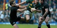 Jean De Villiers (centre) of South Africa is tackled by Dan Carter (left) of New Zealand during their Tri-nations match at Newlands Stadium in Cape Town  6 August 2005. South Africa won 22-16. (Photo: EPA / Nic Bothma)