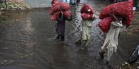 Labourers carry sacks of potato as they wade amid a flooded market in Lahore on 29 August 2022. (Photo: Arif Ali/AFP/Getty Images)
