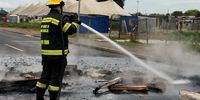 Members of the City of Cape Town's Fire and Rescue Service put out the fires blocking Voortrekker Road at the service delivery protest on Monday 15 September. (Photo: Tamsin Metelerkamp)