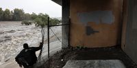 A man who said he has been experiencing episodic homelessness watches water flow in the Los Angeles River, swollen by storm runoff, on October 14, 2025 in Los Angeles, California. A strong atmospheric river storm is hitting Southern California today triggering evacuation warning in the Eaton and Palisades fire burn areas due to debris flow fears.  (Photo: Mario Tama/Getty Images)