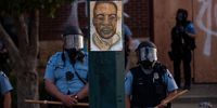 MINNEAPOLIS, MN - MAY 27: A portrait of George Floyd hangs on a street light pole as police officers stand guard at the Third Police Precinct during a face off with a group of protesters on May 27, 2020 in Minneapolis, Minnesota.  The station has become the site of an ongoing protest after the police killing of George Floyd. Four Minneapolis police officers have been fired after a video taken by a bystander was posted on social media showing Floyd's neck being pinned to the ground by an officer as he repeatedly said, "I can’t breathe". Floyd was later pronounced dead while in police custody after being transported to Hennepin County Medical Center.  (Photo by Stephen Maturen/Getty Images)