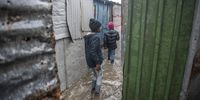 In the pouring rain children walk between their homes in Site B Khayelitsha which were were flooded due to blocked drains. (Photo: Brenton Geach)