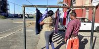 In front, Leanne Pienaar hangs up her washing in Clarke Estate in Cape Town while Noel Small stands behind her, on the lookout for gunmen running into the area.<br>(Photo: Vincent Cruywagen)