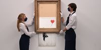 epa09445066 Gallery employees pose for photographers next to a painting entitled 'Love is in the Bin' by anonymous British street artist Banksy at Sotheby's auction house in London, Britain 03 September 2021. The painting was famously shredded by the artist at a Sotheby's auction in 2018 and it is expected to fetch GBP 4-6 million when it goes on sale on 14 October 2021.  EPA-EFE/FACUNDO ARRIZABALAGA