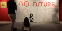 COLOGNE, GERMANY - MAY 09:  A child with her father stand in front of the Banksy work 'No Future' during the exhibition "The Mystery of Banksy - A Genius Mind" on May 09, 2024 in Cologne, Germany.  (Photo by Andreas Rentz/Getty Images)