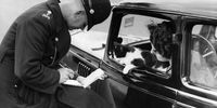 9th October 1936:  A policeman checks a motorist's driving licence while her cat looks on out of the car window.  (Photo by Fox Photos/Getty Images)