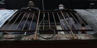 Two men stand on a balcony watching the activities at the bottom of the flats.<br>Photo / Shiraaz Mohamed