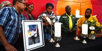 Asange Mchana (centre), the widow of murdered long-distance bus driver Bangikhaya Machana, lights a candle during memorial service at the Intercape Depot in Cape Town. Standing next to her on the right is Machana’s father, Nkululo Mchana. Mchana died after being shot outside his workplace. (Photo: Xabiso Mkhabela)