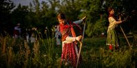 A girl in a tratidional working outfit, uses a scythe to cut meadow in the early morning in Stromovka park, in the city center in Prague, Czech Republic, 02 June 2023. About thirty locals gathered to scythe flower meadow in the biggest Prague's city park.  EPA-EFE/MARTIN DIVISEK