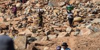 Residents walk over rocks and mud where their homes once stood.