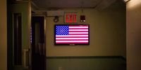 A monitor displays the American flag under an exit sign at the New York Stock Exchange (NYSE) in New York, U.S., on Friday, Nov. 11, 2016. U.S. stocks fluctuated in whipsaw trading, with the Dow Jones Industrial Average spinning near a record, as investors speculate how Donald Trump's policies will impact the economy and interest rates. Small caps headed for the best weekly gain in five years. Photographer: Michael Nagle/Bloomberg via Getty Images