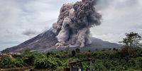 KARO, NORTH SUMATRA, INDONESIA - JUNE 17: A local farmer sits on her fields as Mount Sinabung spews pyroclastic smoke, seen from Tiga Kicat village on June 17, 2015 in Sukanalu village, North Sumatra, Indonesia. According The National Disaster Mitigation Agency, more than 10,000 villagers have fled their homes since the authorities raised the alert status of Mount Sinabung erupting to the highest level. (Photo by Ulet Ifansasti/Getty Images)